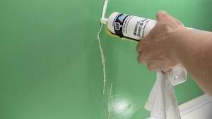 photo filling a plaster wall crack with caulk