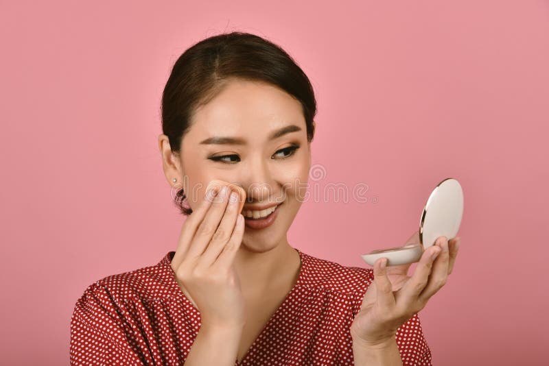 Asian woman applying makeup cosmetics while looking at the mirror, Midday face powder foundation touch up to keep looking fresh. stock photography