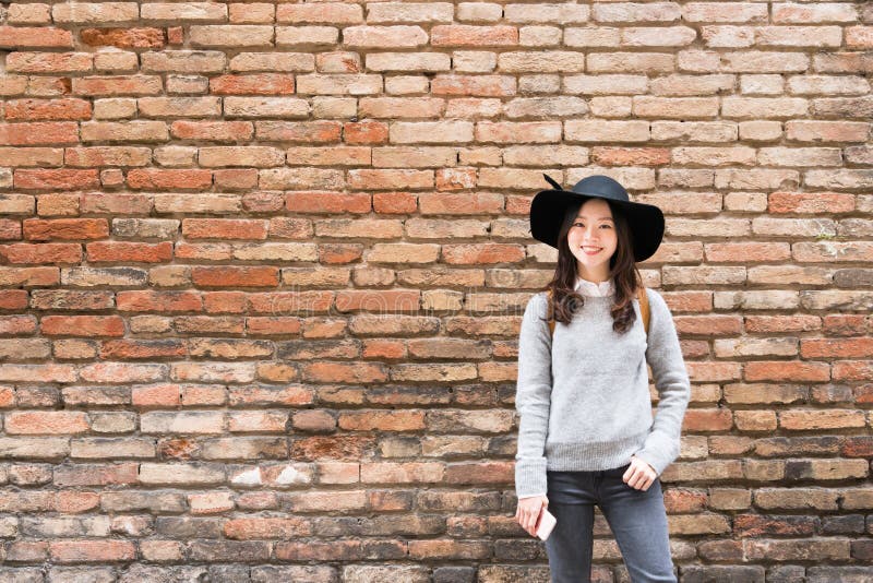Beautiful asian girl in fashionable dress, standing in front of red brick wall background with copy space stock image
