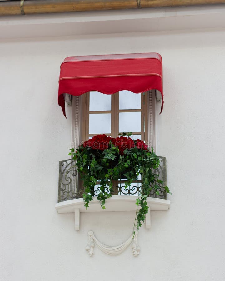 Beautifully decorated window, French balcony with red flowers and a canopy. White wall of a house with a flower pot and molding. Architecture design beauty stock photography