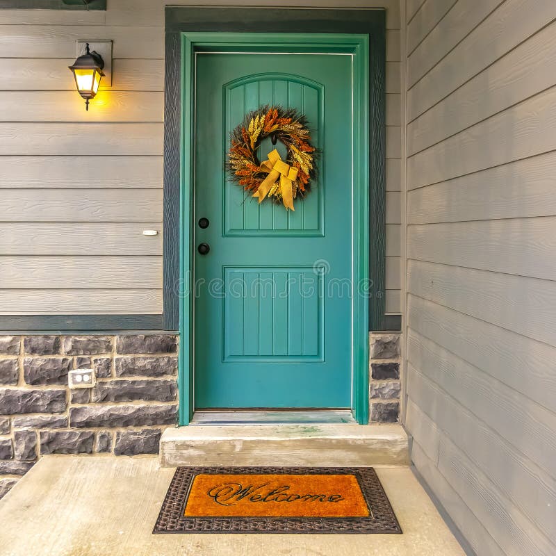 Blue green front door with a welcoming wreath. Holiday wreath hanging on the beautiful blue green front door of a house. A welcome doormat and wall lamp can royalty free stock photography