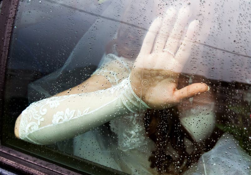 The bride put her hand on the window glass covered with raindrops stock image