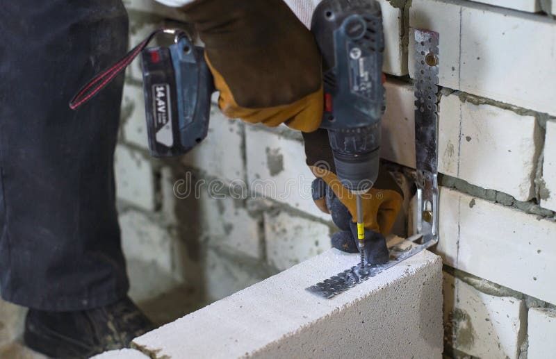 Builder screwing joining clamp in aerated concrete block with electric drill. Worker building interior wall at construction site. house renovation, building royalty free stock images