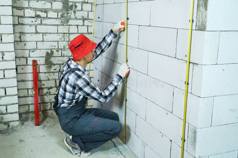 Builder sitting on his hunkers installing metal rails onto clamps on block wall. Builder sitting on his hunkers installing metal rails onto clamps on aerated royalty free stock photos