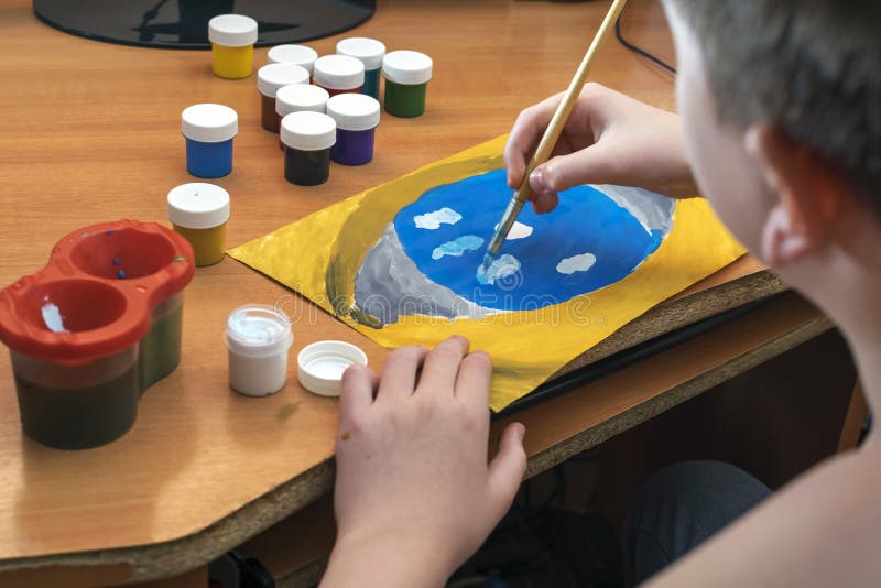 The child draws gouache on a sheet and jars of paint are on the table. royalty free stock image