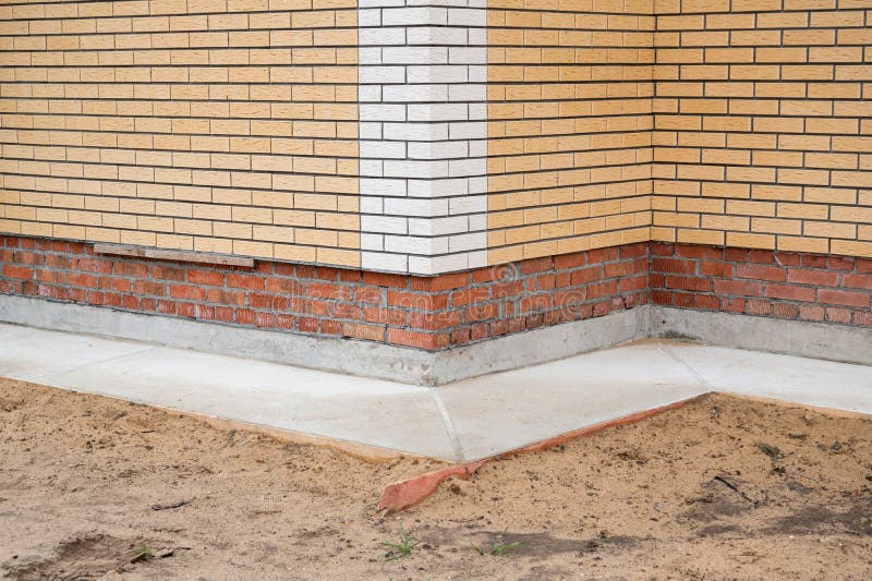 Corner of new brick house faced by decorative brick tile and with concrete blind area. Closeup view royalty free stock image