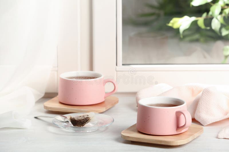 Cups of hot tea with wooden coasters. On window sill royalty free stock image