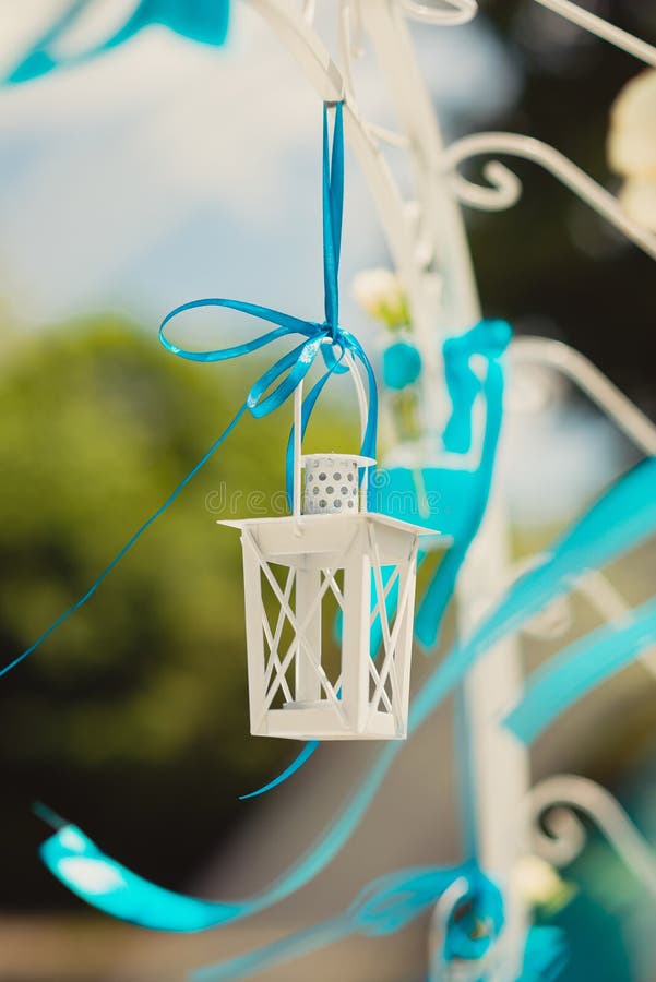 Decorative white lantern for candles on decorative white arch on a blue ribbon tied on a background of green leaves. And blue sky royalty free stock image