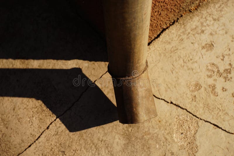 Downpipe at the corner of the building, cracks in the blind area of the house, sunlight and shadow from the drain pipe. Downpipe at the corner of the building royalty free stock images