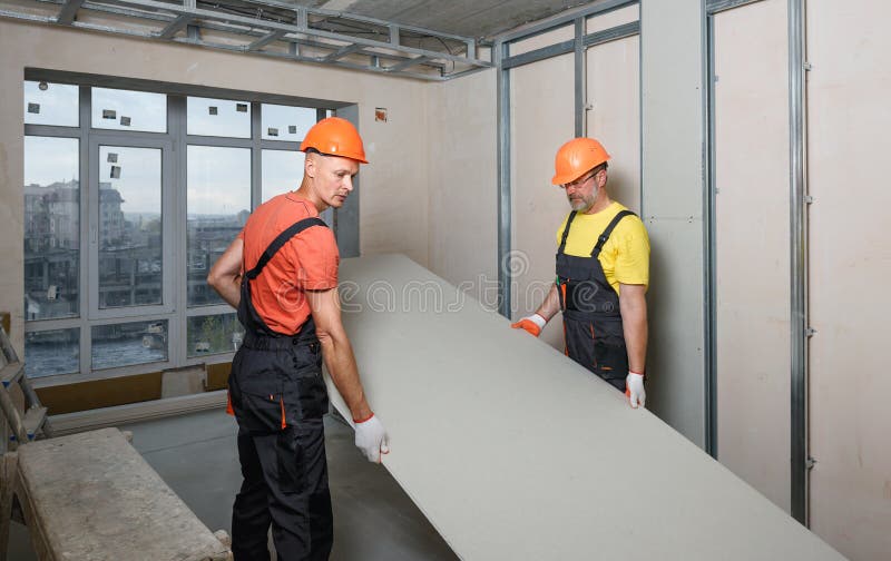 Drywall installation on the wall. Workers are carrying plasterboard for further attachment to the wall royalty free stock images