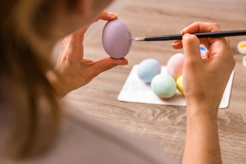 Easter mood. close up young woman hands painting easter eggs with brush and gouache in pastel colors over wooden table at home royalty free stock photo