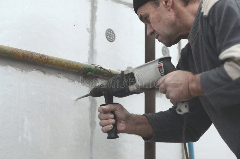 An elderly workman drills a hole in a styrofoam wall for the subsequent installation of a plastic reinforcing dowel. Creating royalty free stock photography