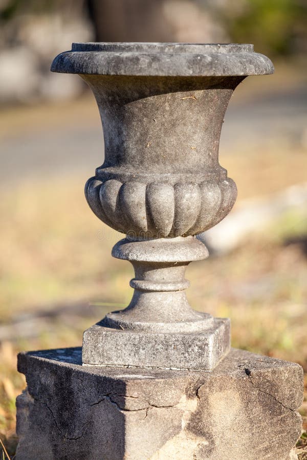 Empty old concrete or stone urn on a small plinth. Discolored ornamental stone or concrete urn in the sunlight on a small plinth royalty free stock photos