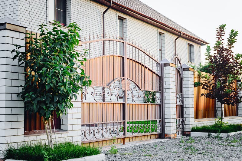 A brown fence made of polyprofile with a canopy in a modern style with brick columns, the design of a country house. A fence made of polyprofile with a canopy in royalty free stock photography