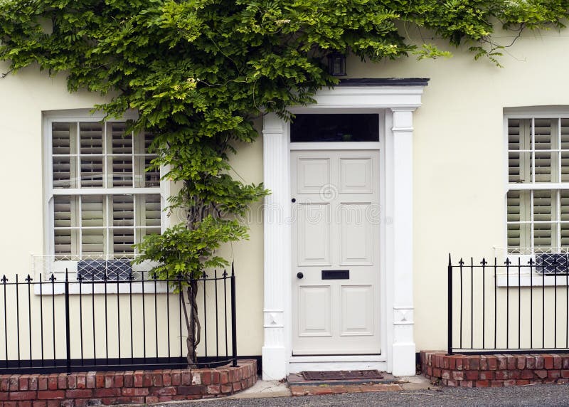 Front door. White front door entrance and old style window of a white house or a cottage with green wall plant and iron fence royalty free stock photo