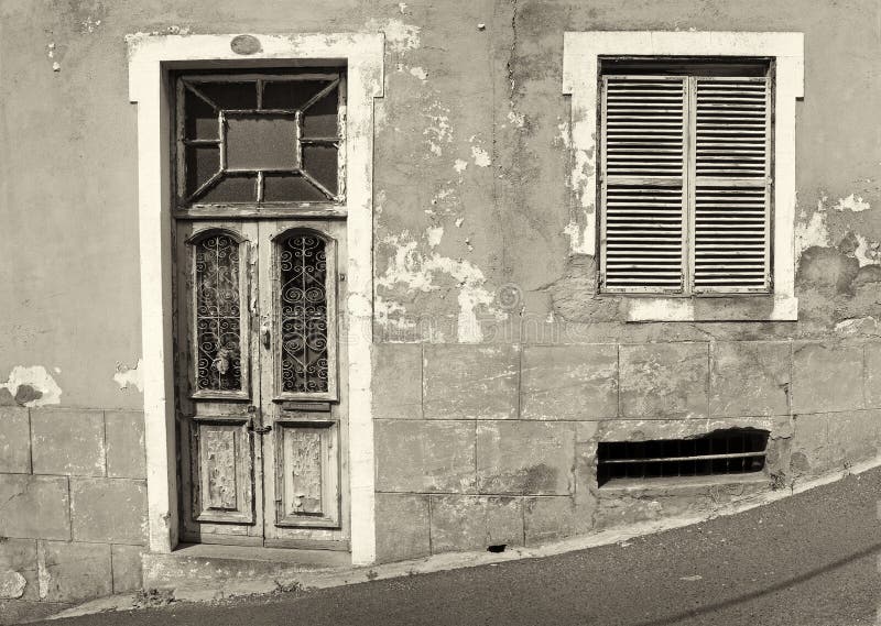 The front of an old abandoned house with shuttered windows and locked wooden door with flaking peeling paint on a sloping street. Monochrome image royalty free stock images