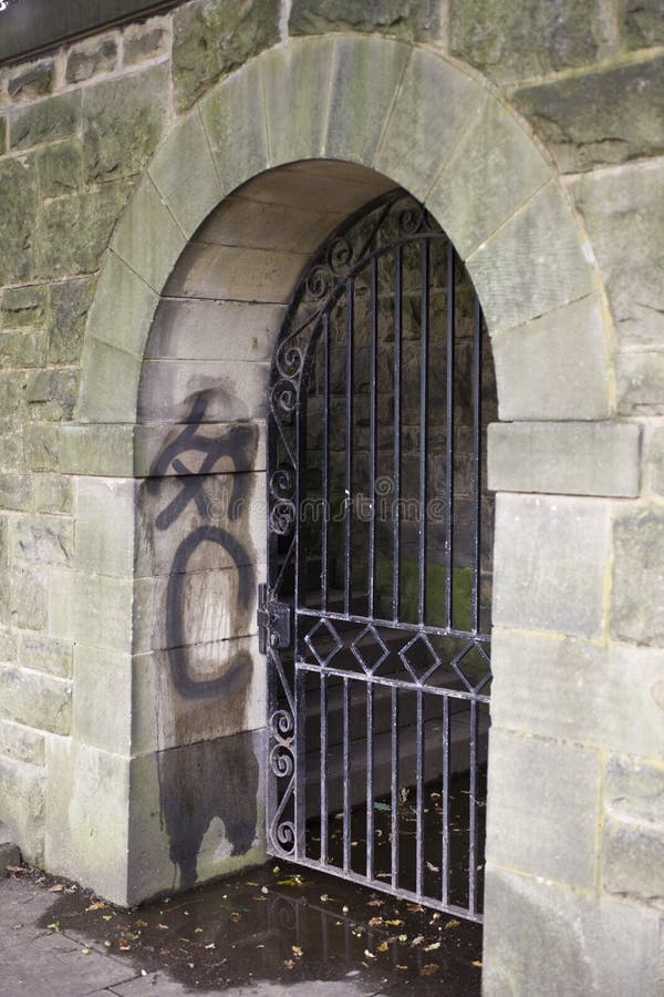 Gated Doorway with Graffiti. Decorative arched wrought iron gate in an old block stone doorway. Graffiti on inside of of doorway to the left royalty free stock image