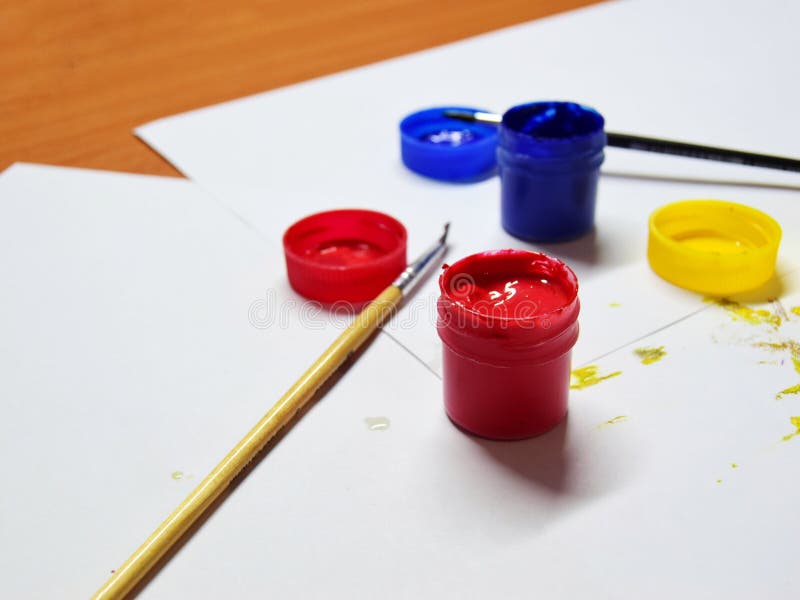 Gouache for drawing in different colors, brushes and children`s drawings on a wooden table. close-up. selective focus stock image