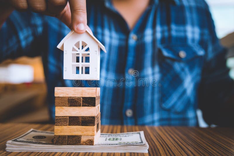 Hand holding a piece of wood block with model white house on dollar banknote. Insurance and property investment real estate. Concept stock photography