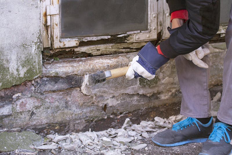 Hand of worker with gloves hammering down plaster on facade that crumbles due to moisture and mold underneath a white wooden frame stock images