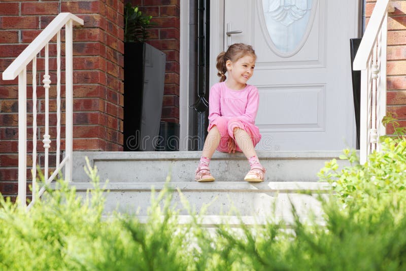 Happy girl sits on stairs near door, smiles royalty free stock images