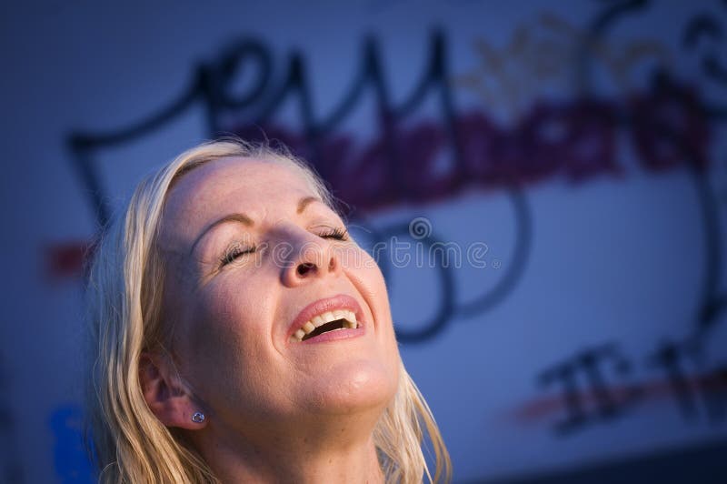 Head of blond woman and graffiti. Head view of a blond woman of middle age to sloping head, eyes closed and half open mouth in front of blue wall with sex royalty free stock images