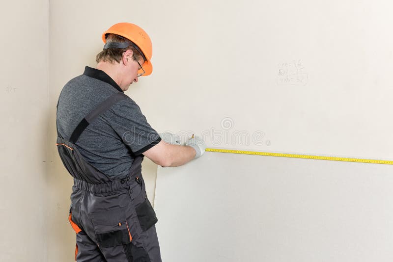 Installation of drywall. The worker is measured to cut plasterboard. Installation of drywall. The worker is measured to cut off a piece of drywall later stock image