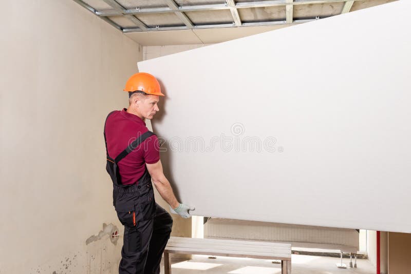 Workers are using screws and a screwdriver to attach plasterboard to the ceiling. Installation of drywall. Workers are using screws and a screwdriver to attach royalty free stock photo