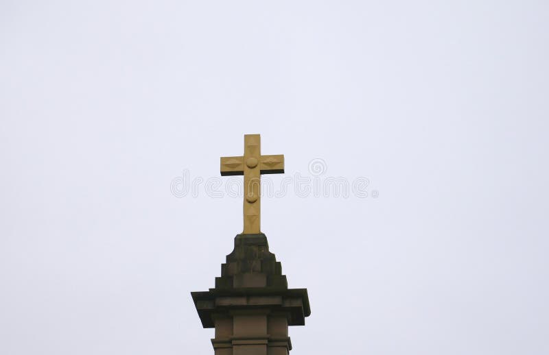 Large gold coloured cross on stone plinth. With diamond and circular designs royalty free stock photo