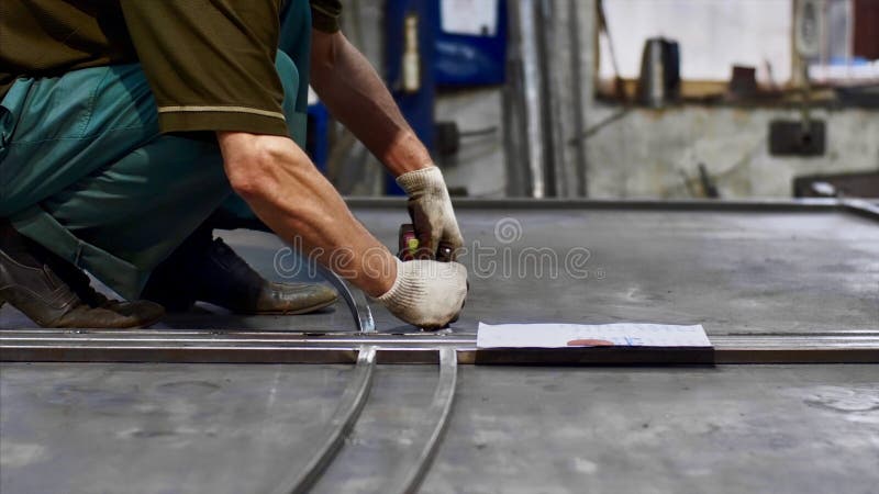 Locksmith measures tape measure length of metal bars and makes marks in workshop. Man worker locksmith measures tape measure length of metal bars. He makes marks stock photos