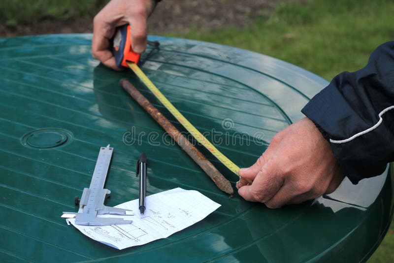Man measures metal rod length with roulette. Nearby is caliper, pen and paper sheet stock photo
