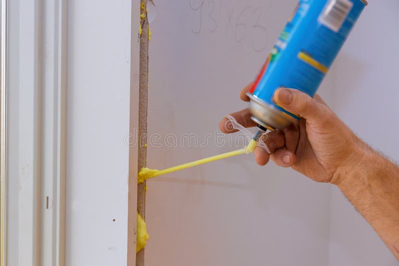 Man using polyurethane foam for installing a window on a handsome worker in action royalty free stock image