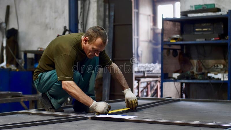 Locksmith measures tape measure length of metal bars and makes marks in workshop. Man worker locksmith measures tape measure length of metal bars. He makes marks stock photos
