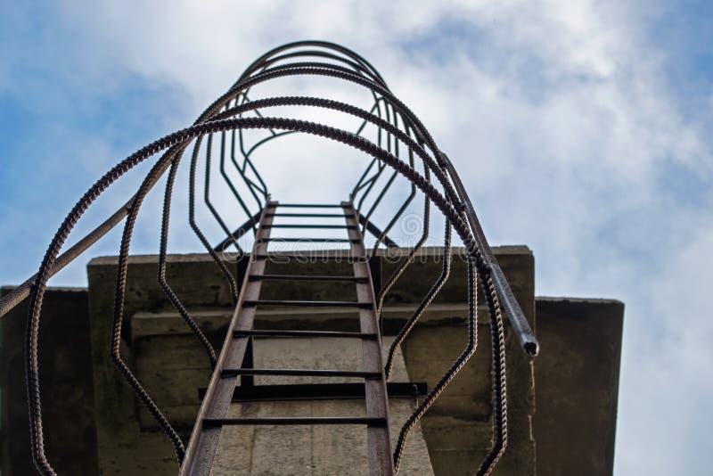 Metal ladder running vertically from bottom up over concrete angular structure with ribbed safety iron holders along entire length. A metal ladder running stock photography