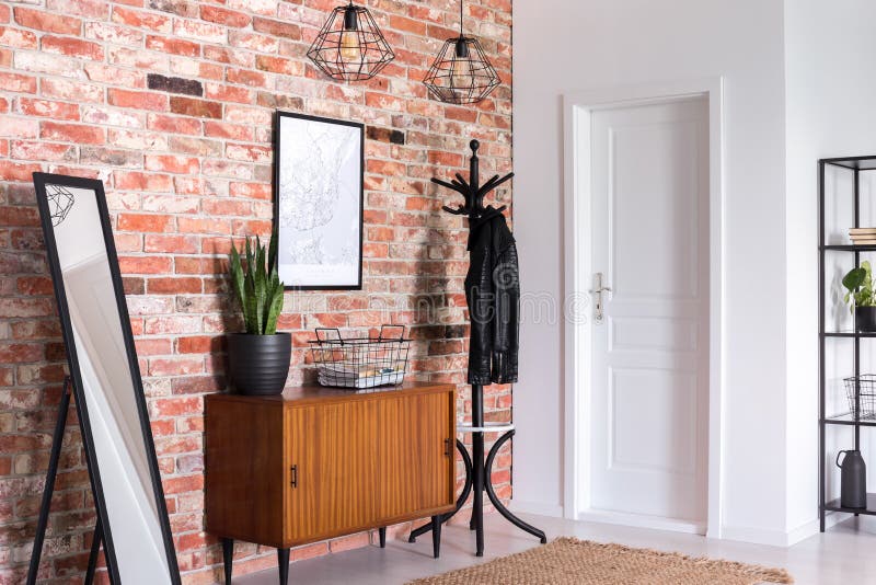 Mirror next to wooden cabinet in entrance hall interior with white door and poster on red brick wall stock photos