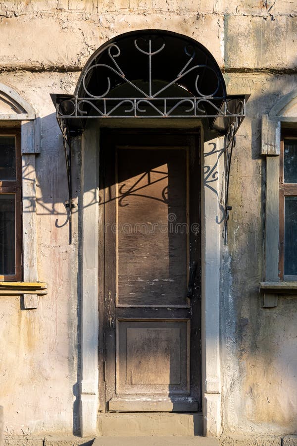 Narrow old wooden door with peeling brown paint. Metal rain canopy with curly patterns of metal rods. Abandoned house.  royalty free stock images