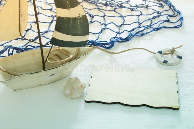Nautical concept image with white decorative sail boat and empty wooden board over white table. Nautical concept image with white decorative sail boat and empty stock photo