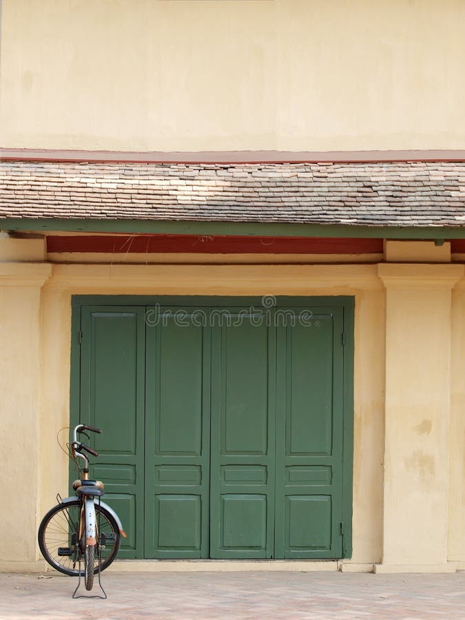 Old rustic abandoned retro style bicycle parked at historic vintage beige colour building facade. With green painted wooden door in a small peaceful lovely stock images