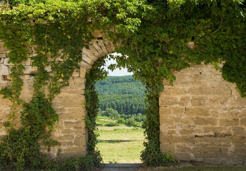 Old wall with arch. Closeup of ivy covered old stone wall with landscape view through the arch royalty free stock images