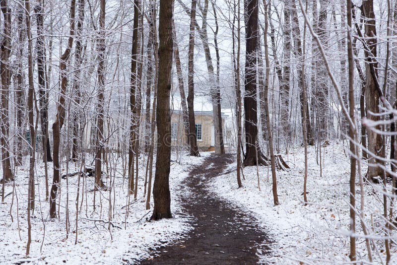 Path in wooded area covered in a light late spring fresh snow fall with a small yellow brick cottage in the background stock images