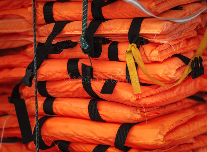Pile of life-jackets ready for shipping. Close-up view of packed orange life-jackets pile ready for shipping. String with hook holding jacket. Safety control on royalty free stock photos
