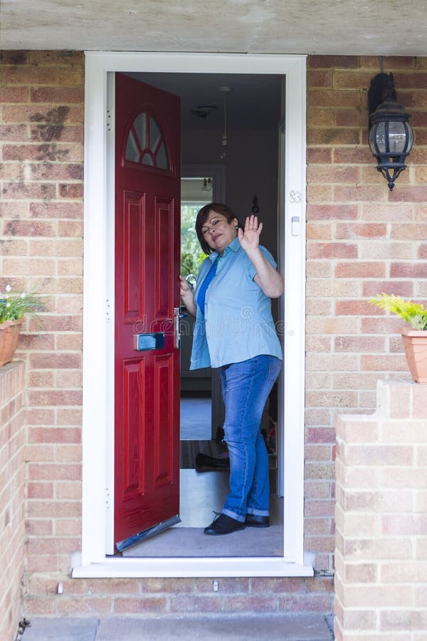Portrait of happy mature woman at front door. Happy middle aged woman opening front door and smiling royalty free stock photo