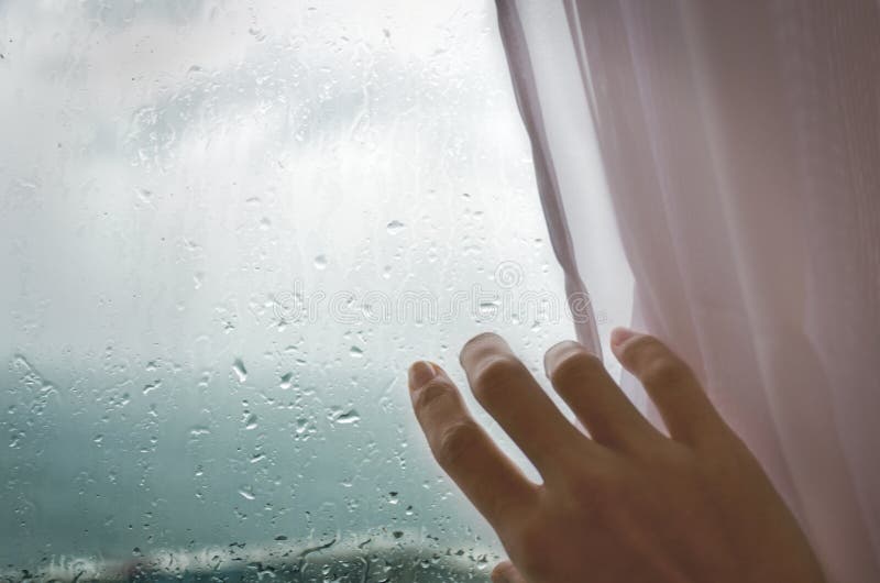 Rainy weather - a woman`s hand pulls the blind from the rainy window. stock images