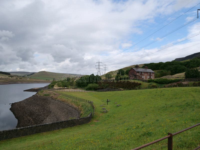 Red brick cottages by Reservoir with very low water. Red brick cottages by Muddy banks of Reservoir with very low water with mud banks trees electricity pylons stock photo