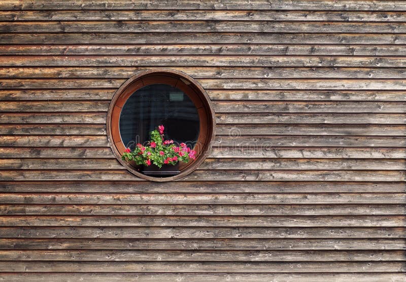 Round window with a geranium flower pot on  rustic wooden facade. Background and texture stock image