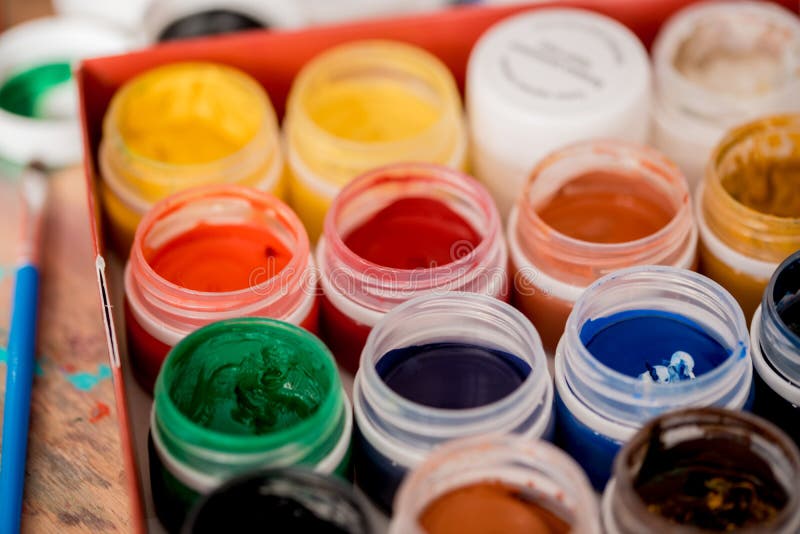 Set of nine colors gouache paints in jars on wooden table. Focus on red stock image