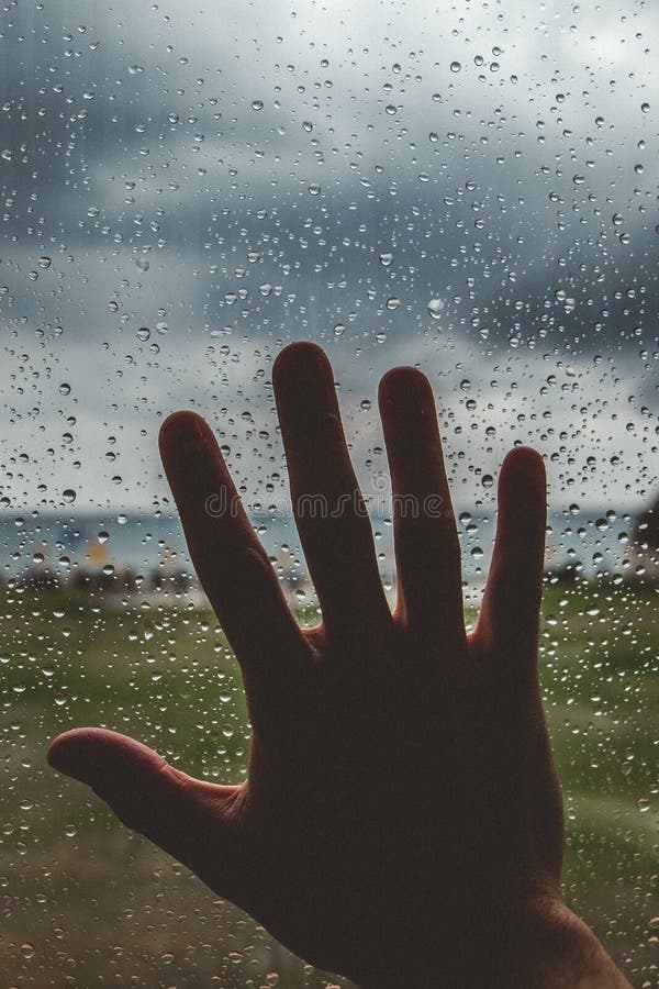 Silhouette of a hand touching a window full of water drops stock photos
