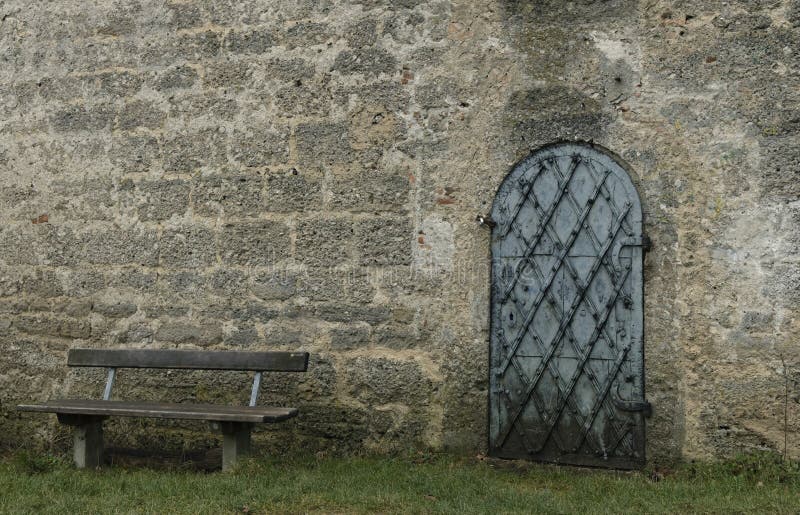 Soft focus stone castle wall background with iron arch shape door and empty bench European landmark. View stock photography