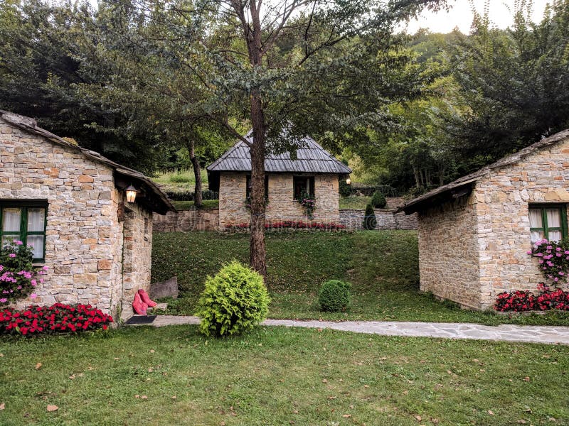 Three stone rustic cozy mountain village houses with colorful flowers and brick stone facade surrounded by green grass and nature. Summer sunny day royalty free stock image