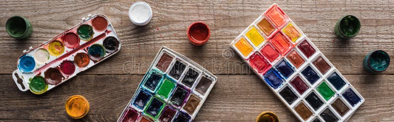 Top view of colorful paint palettes on wooden brown table with gouache, panoramic shot. stock photo